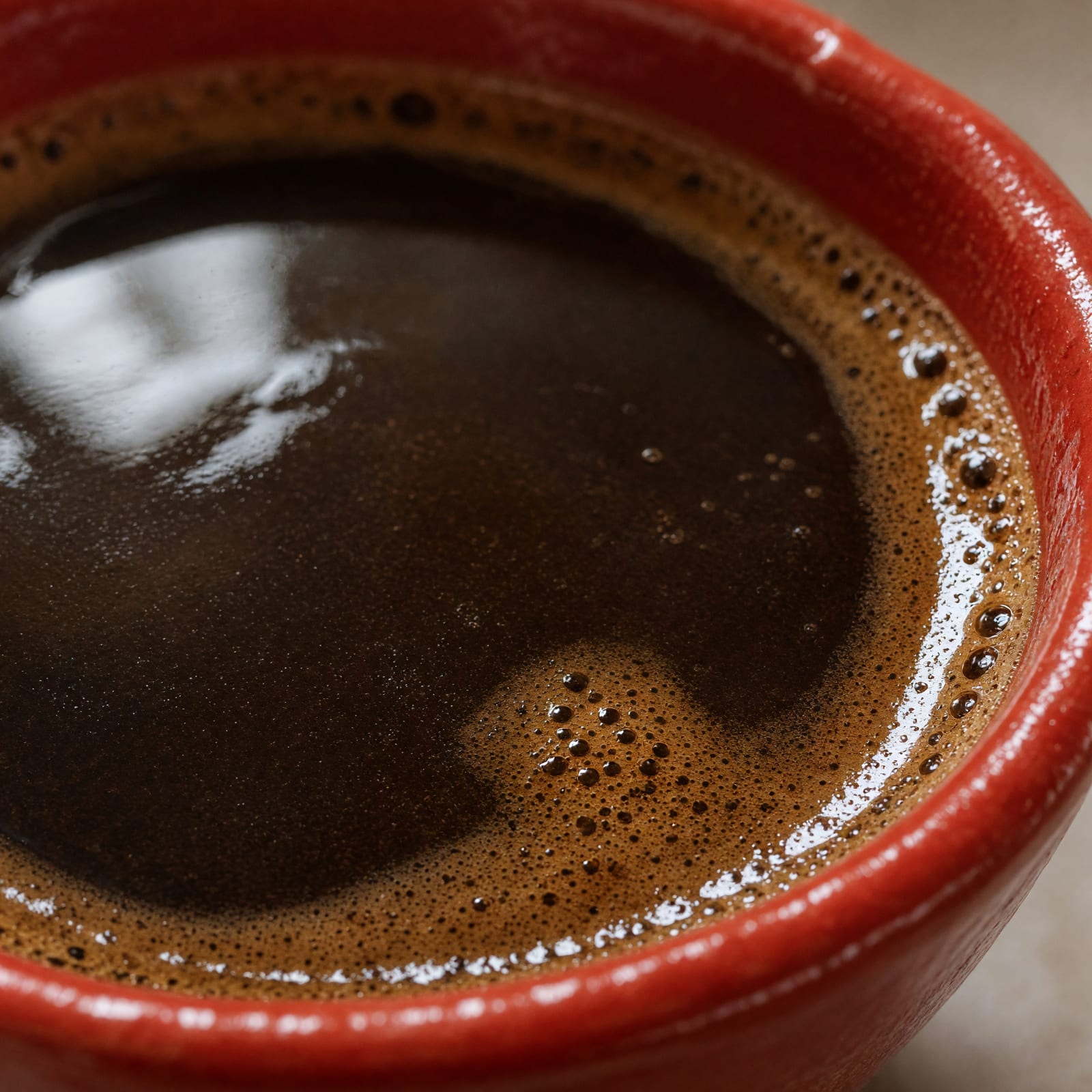Blick in eine rote Keramiktasse auf die dunkle Kaffeeoberfläche mit feinem Rand und wenigen Bläschen.